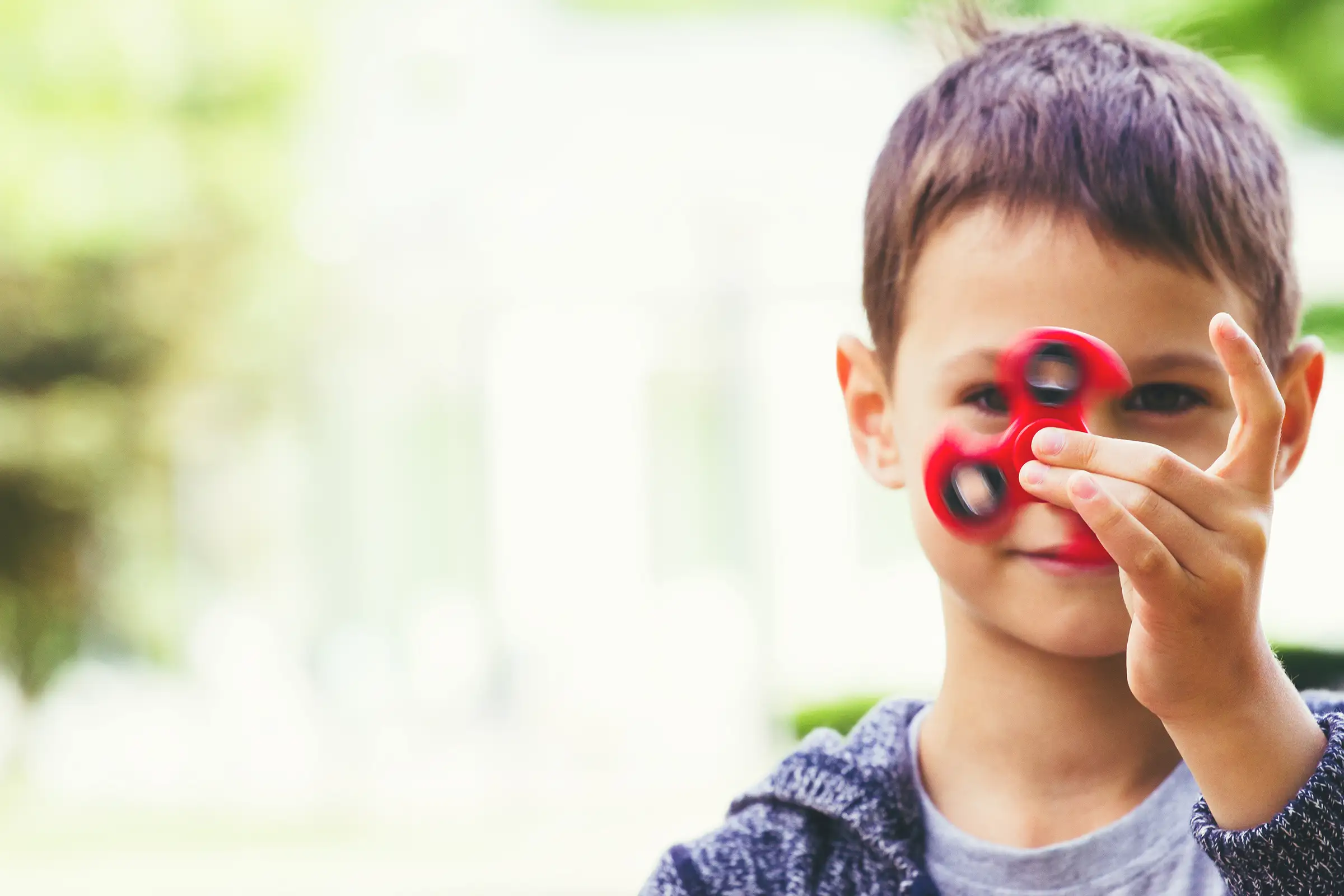 Boy holding a fidget spinner moving quickly, his eye visible behind his hand