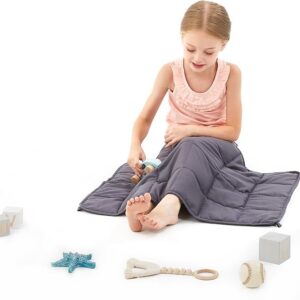 girl sitting on ground with grey quilted blanket on lap