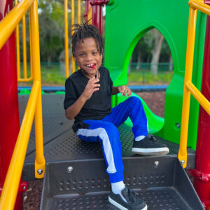 child on a playground seated chewing on necklace