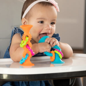 baby in high chair with one toy in each color on her tray