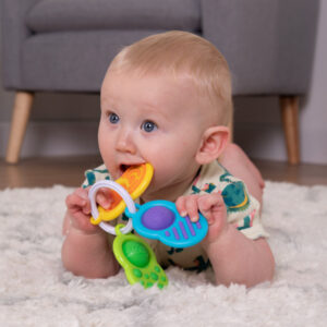 baby on tummy holding white ring with 3 different flat pieces with sensory textures