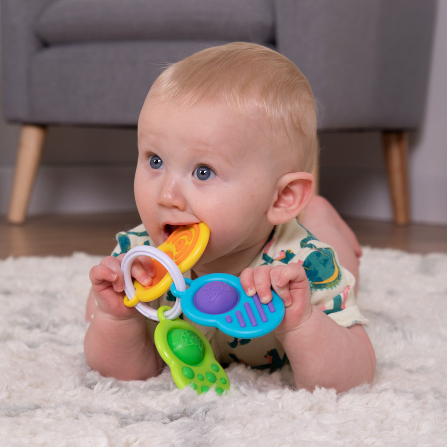 baby on tummy holding white ring with 3 different flat pieces with sensory textures