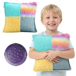 A young boy holds a square pillow that has fuzzy rainbow, blue, and yellow fabric