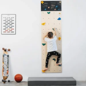 light wood wall with screw holes with multi colored climbing holds, shown with child climbing up and safety mat below