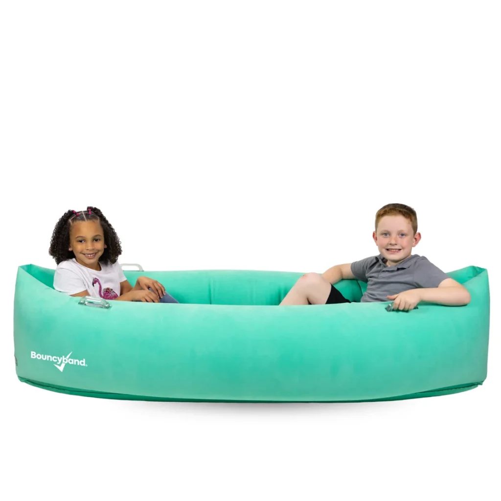two children in a mint green canoe-shaped pod smiling at camera