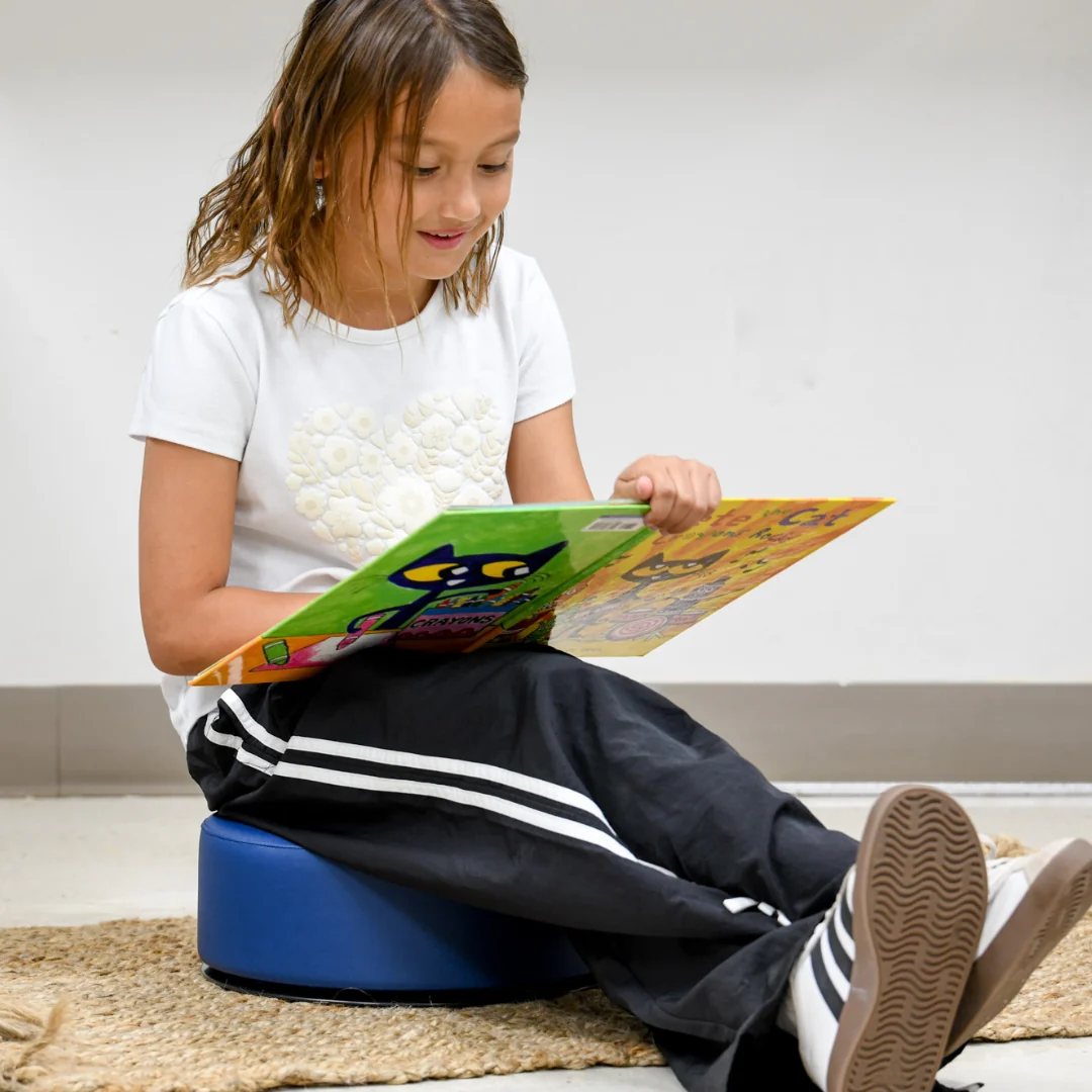child reading while sitting on blue seat with legs stretched out