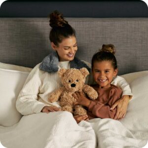 mom and girl in bed holding tan colored teddy bear