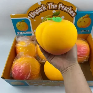 a hand holds a peach colored and shaped squishy with green leaves in front of a display case of plastic wrapped peach squishy toys