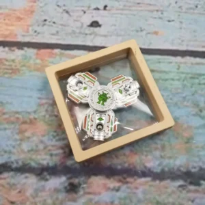 silver metal 3-pronged spinner with green robot at center in clear box with beige frame