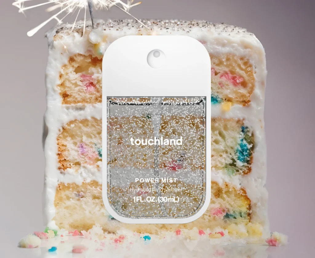 rectangular bottle with clear panes and white frame of clear liquid with silver glitter. Slice of confetti cake in background