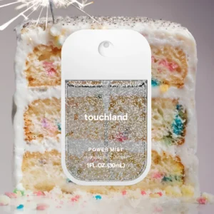 rectangular bottle with clear panes and white frame of clear liquid with silver glitter. Slice of confetti cake in background
