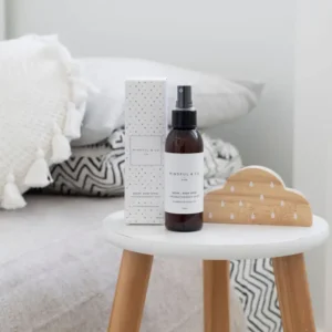 brown bottle with spray mist top shown with white box on a nightstand next to a bed
