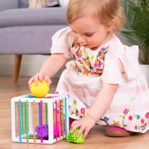 toddler pushing a yellow sphere through the multicolored elastic bands on a White cube