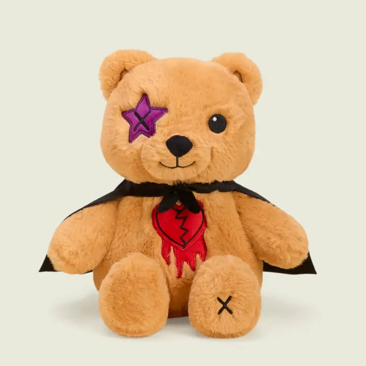 tan teddy bear with star "X" eye, cape and broken heart patch