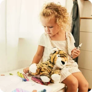 a girl sits by a window coloring with her striped tiger at her side