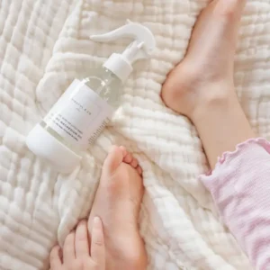 clear spray bottle next to feet on a bed with a cream colored blanket